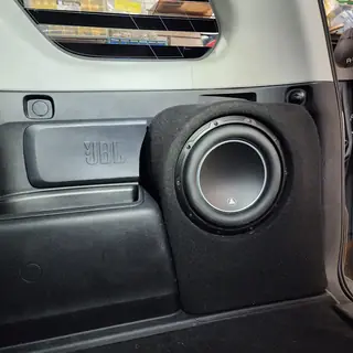 Subwoofer in a carpeted enclosure beside a factory JBL-labelled rear panel